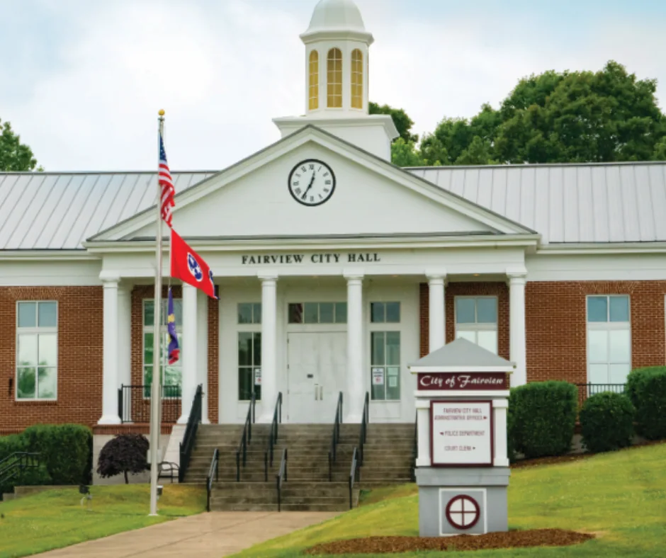 Fairview City Hall building with clock tower, American and Tennessee flags, and landscaped entrance in Fairview, Tennessee.