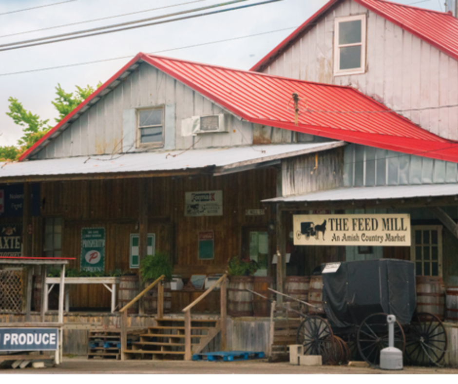 Amish country market "The Feed Mill" in Nolensville, featuring a wooden facade, red metal roof, and horse-drawn carriage, surrounded by greenery and local produce signs.