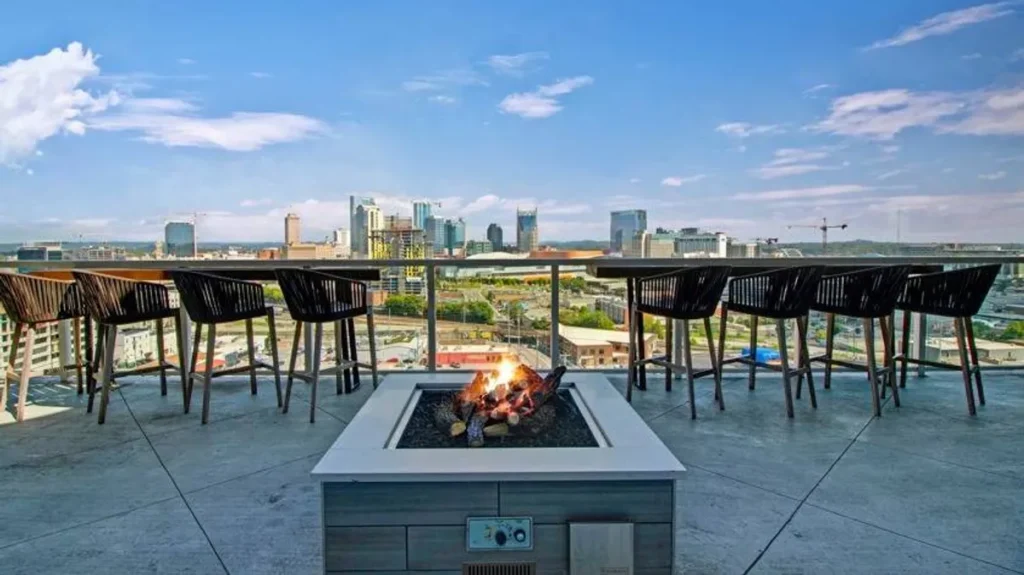 Rooftop patio with fire pit overlooking Nashville skyline, featuring modern seating and vibrant urban landscape in The Gulch neighborhood.