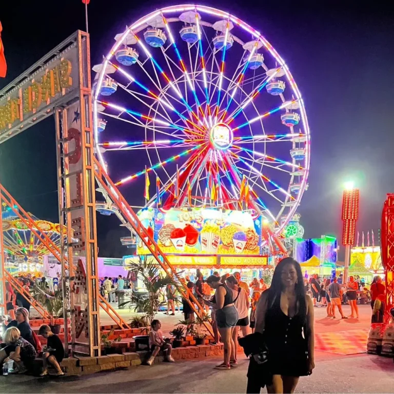 Ferris wheel illuminated with colorful lights at a lively fair in Lebanon, Tennessee, with people enjoying the festive atmosphere and various food stalls.