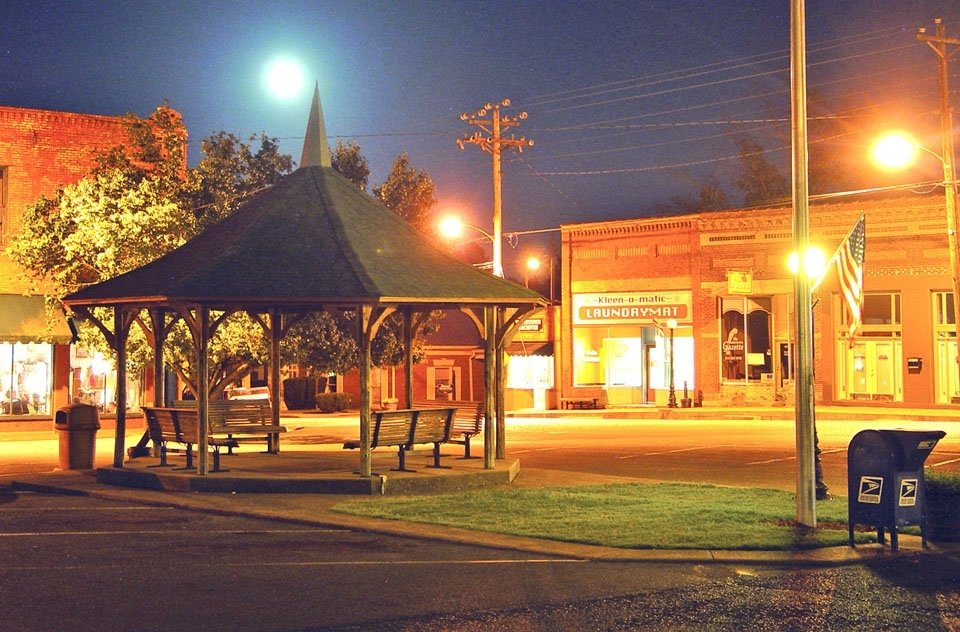 Gazebo in Watertown, Tennessee, illuminated at night, surrounded by historic buildings, featuring a laundromat and American flag, emphasizing the town's charm and community atmosphere.