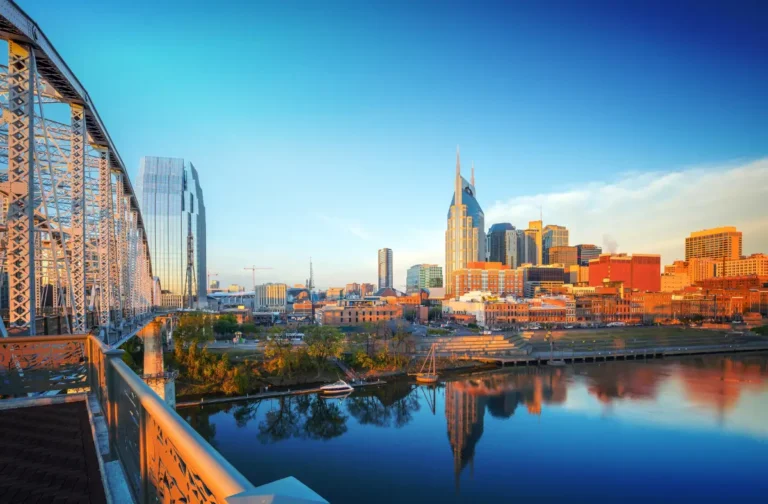 Nashville skyline at sunset featuring the AT&T Building and vibrant cityscape along the Cumberland River, showcasing the local real estate landscape.